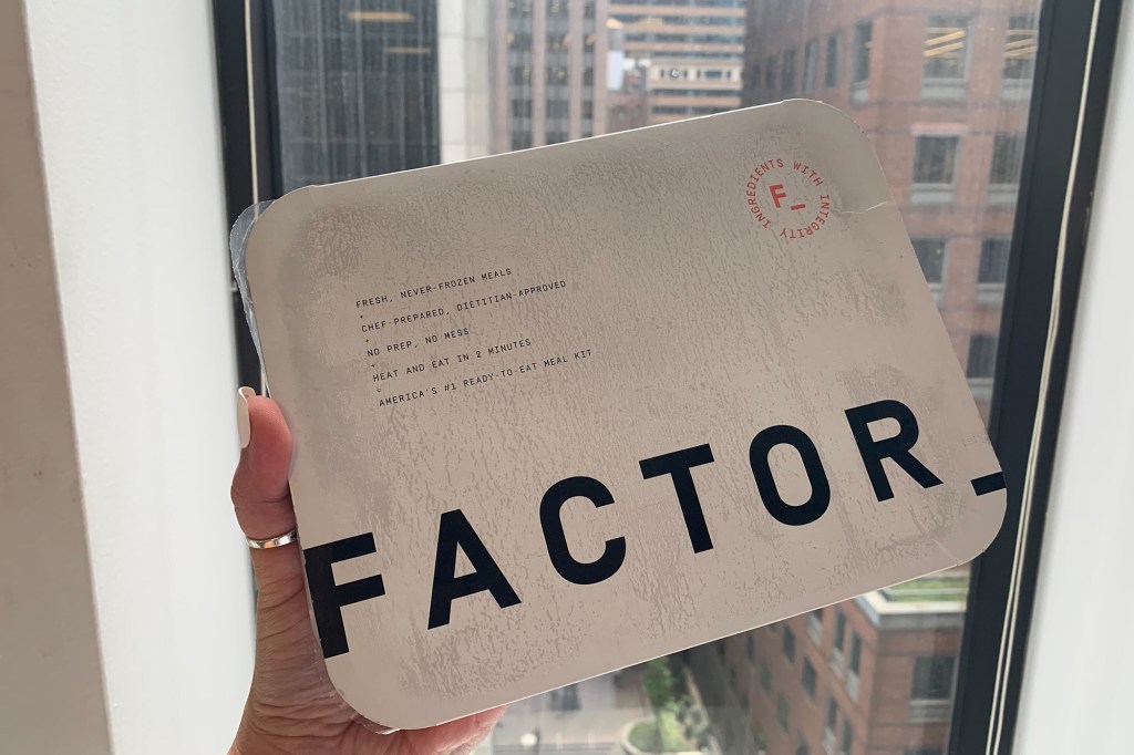 A hand holding a box of Factor over a window 